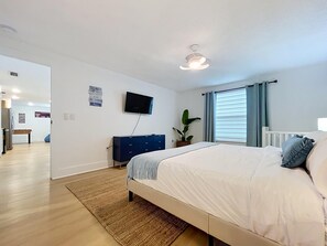 Ein Schlafzimmer mit einem Bett, einem Schminktisch, einem Fernseher und einer Pflanze.