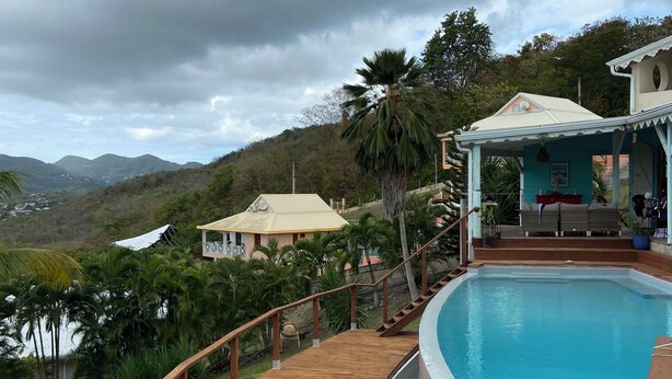 Ein Pool mit Holzterrasse, einer überdachten Sitzgelegenheit und Blick auf Hügel und einen See.