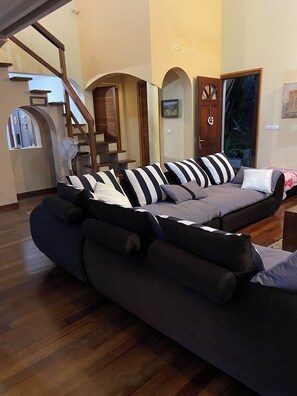 A modern living room with a sectional sofa, wooden flooring, and a staircase. - Villa Le Diamant (le diamant)