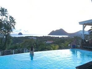 A person in a swimming pool with a view of a mountain and a body of water. - Villa Le Diamant (le diamant)