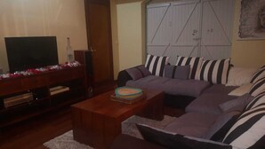 Ein Wohnzimmer mit einem Ecksofa, einem Couchtisch, einem Fernseher und einer Tür.