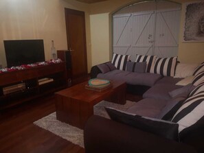 A living room with a sectional sofa, a coffee table, a television, and a door. - Villa Le Diamant (le diamant)