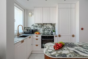 A modern kitchen with white cabinetry, a marble countertop, and a built-in oven. - Family Stay in Warsaw (Warsaw)