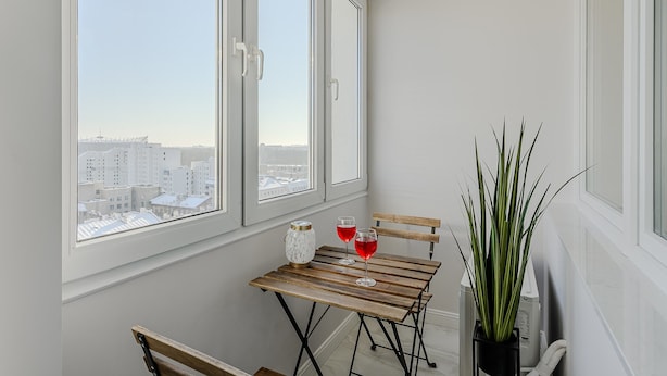 A balcony with a view of a cityscape, a wooden table with two glasses of red liquid, and a potted plant. - Family Stay in Warsaw (Warsaw)