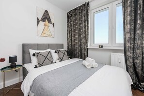 Um quarto moderno com uma cama, um criado-mudo, uma luminária e uma janela com cortinas.