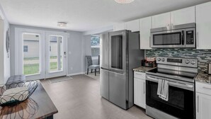 A modern kitchen with stainless steel appliances, a dining area with a table and chairs, and a view of the outdoors through the sliding glass doors.