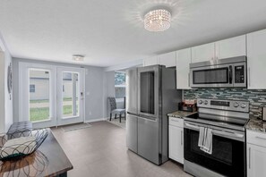 A modern kitchen with stainless steel appliances, a dining area with a table and chairs, and a view of the outdoors through the sliding glass doors.