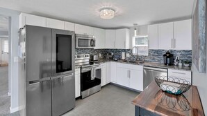 A modern kitchen with stainless steel appliances, white cabinetry, a tiled backsplash, and a contemporary light fixture.
