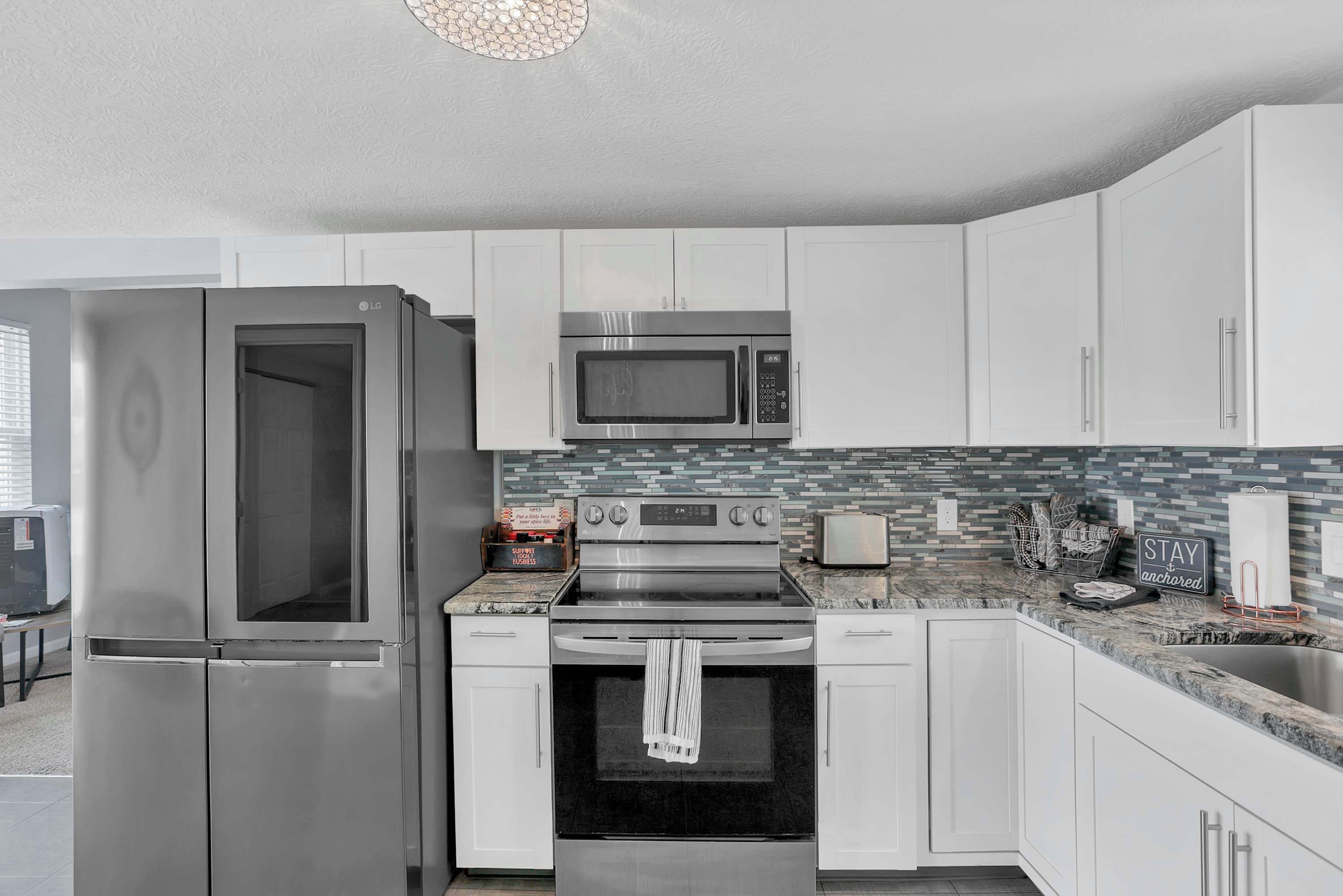 A modern kitchen with stainless steel appliances, white cabinets, a tiled backsplash, and a countertop with a toaster and a basket.