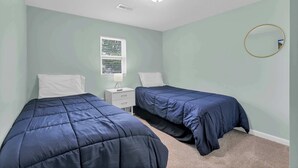 A bedroom with two beds, a window, a nightstand, a mirror, and a ceiling light.