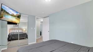A hotel room with a bed, a television mounted on the wall, and a door leading to another room.