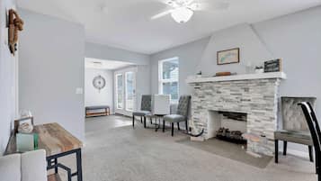 A living room with a stone fireplace, a ceiling fan, and a dining area with a wooden table and chairs.