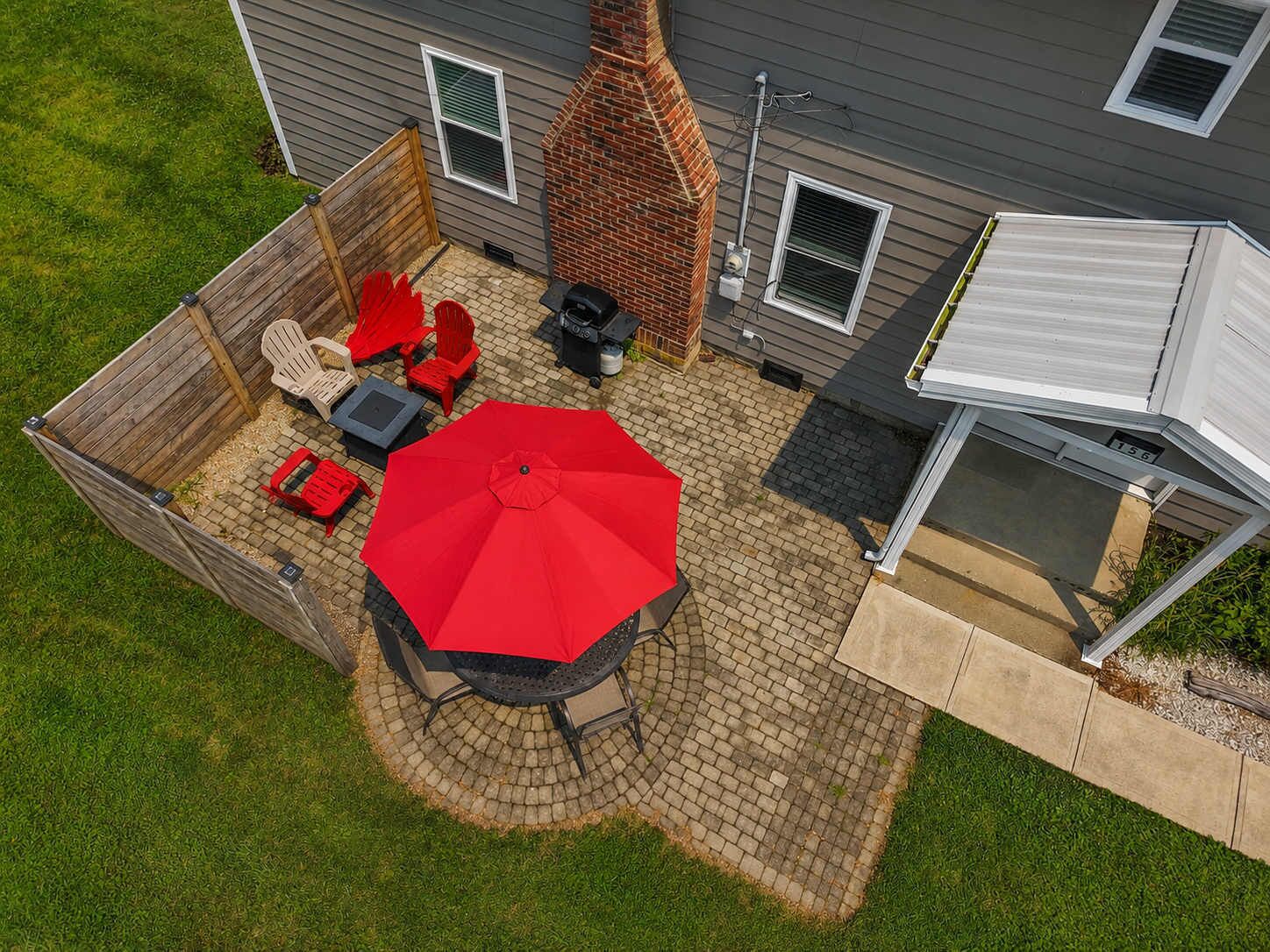 Eine Terrasse mit einem runden Tisch, roten Stühlen und einem roten Sonnenschirm.