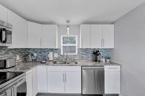 Una cocina moderna con armarios blancos, microondas de acero inoxidable, cafetera y lavavajillas.