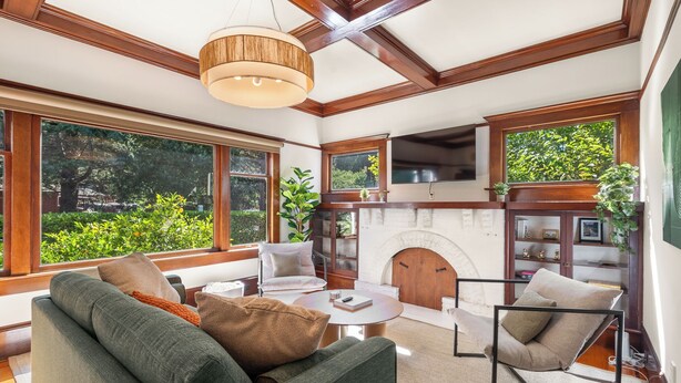 A spacious living room with a fireplace, large windows, and a high ceiling with exposed beams.