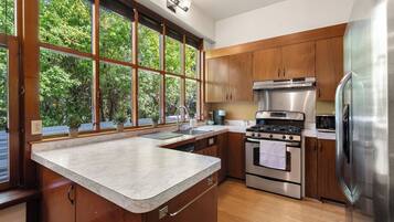 A modern kitchen with wooden cabinets, stainless steel appliances, and a large window overlooking greenery.