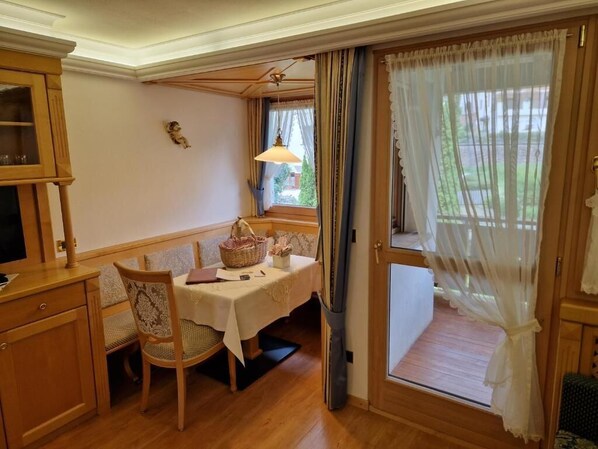 A dining area with a table set for two, a wooden cabinet, and a window with curtains.