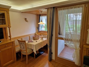 A dining area with a table set for two, a wooden cabinet, and a window with curtains. - Residence Ciastel (Oltretorrente)