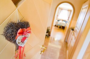 A hallway with a decorative hanging on the wall, a door with a golden handle, and a glimpse of a room with a bed and a window.