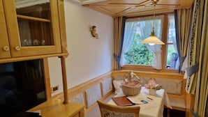 Habitación pequeña con televisión, un armario de madera, una mesa con silla y una ventana con cortinas.