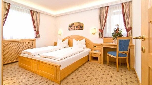 Habitación de hotel con cama doble, un escritorio con silla, mesita de noche y ventana con cortinas.