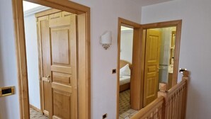 Un pasillo con puertas de madera, una lámpara y un espejo que refleja una habitación con una cama.