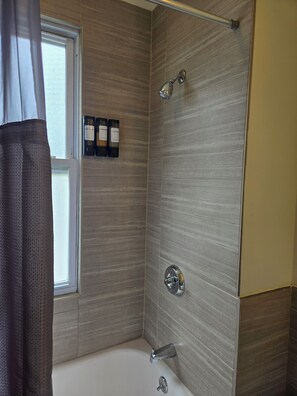 A bathroom with a bathtub, a shower, and a window with curtains.