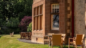A building with a stone facade, large windows, and outdoor seating with chairs and tables. - Dunkeld House - Luxury Cottages (Dunkeld)