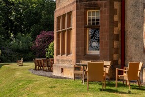 A building with a stone facade, large windows, and outdoor seating with chairs and tables. - Dunkeld House - Luxury Cottages (Dunkeld)