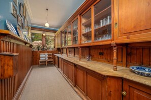 A wooden kitchen with a herringbone floor pattern, a wooden bar counter, and a large window with a view of greenery. - Dunkeld House - Luxury Cottages (Dunkeld)