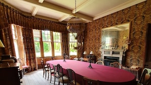 A formal dining room with a long table, chairs, a chandelier, and a fireplace. - Dunkeld House - Luxury Cottages (Dunkeld)