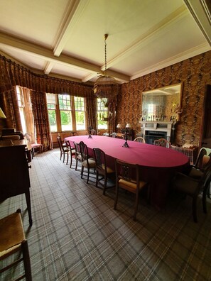 A formal dining room with a long table, chairs, a chandelier, and a fireplace. - Dunkeld House - Luxury Cottages (Dunkeld)