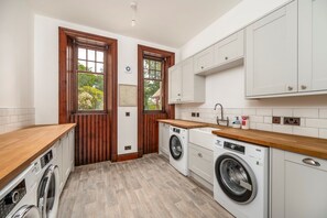 A modern kitchen with wooden cabinets, a washing machine, and a sink. - Dunkeld House - Luxury Cottages (Dunkeld)