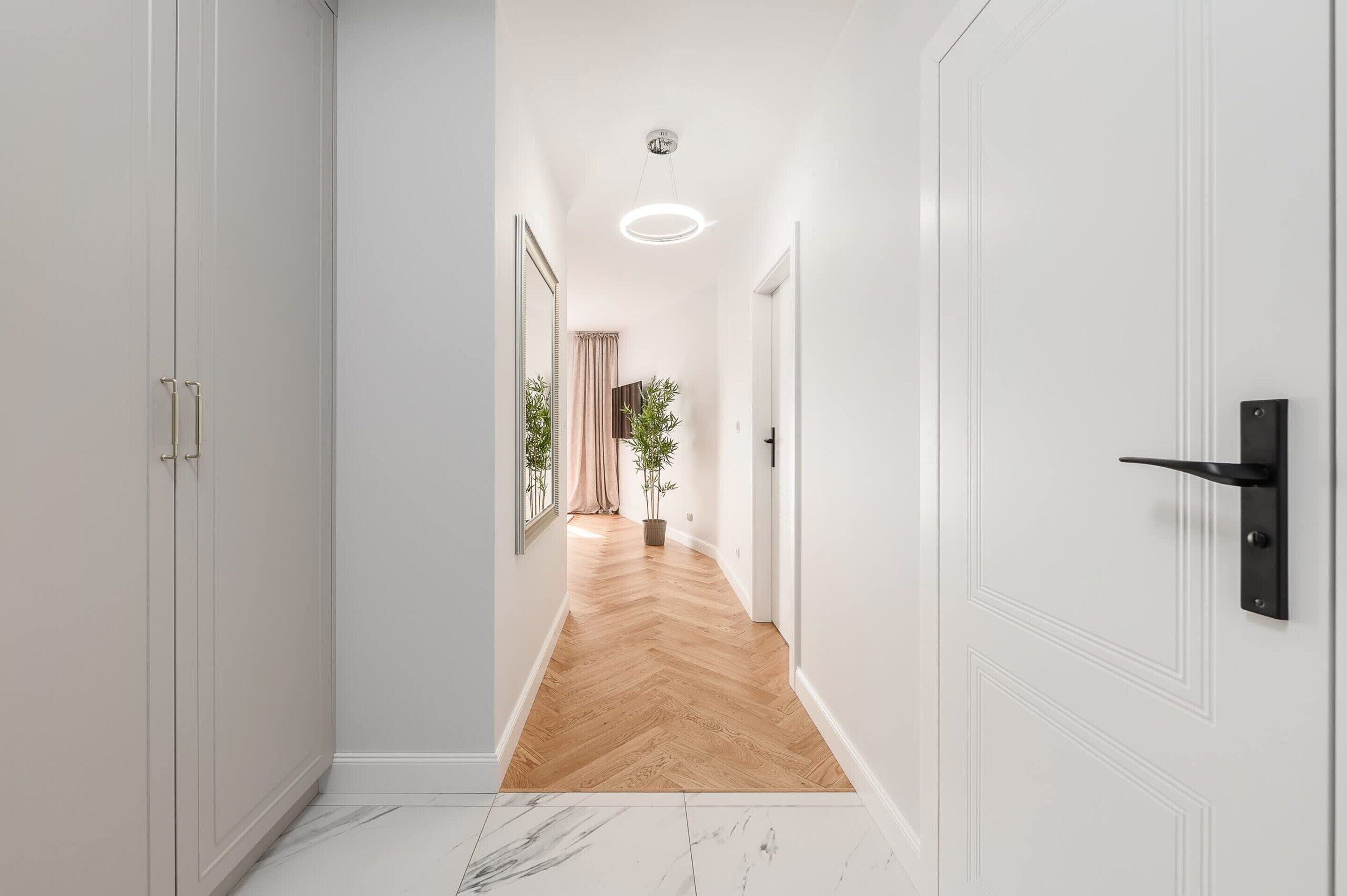 Un couloir aux murs blancs, doté d’un plancher en bois et d’une porte avec une poignée noire.