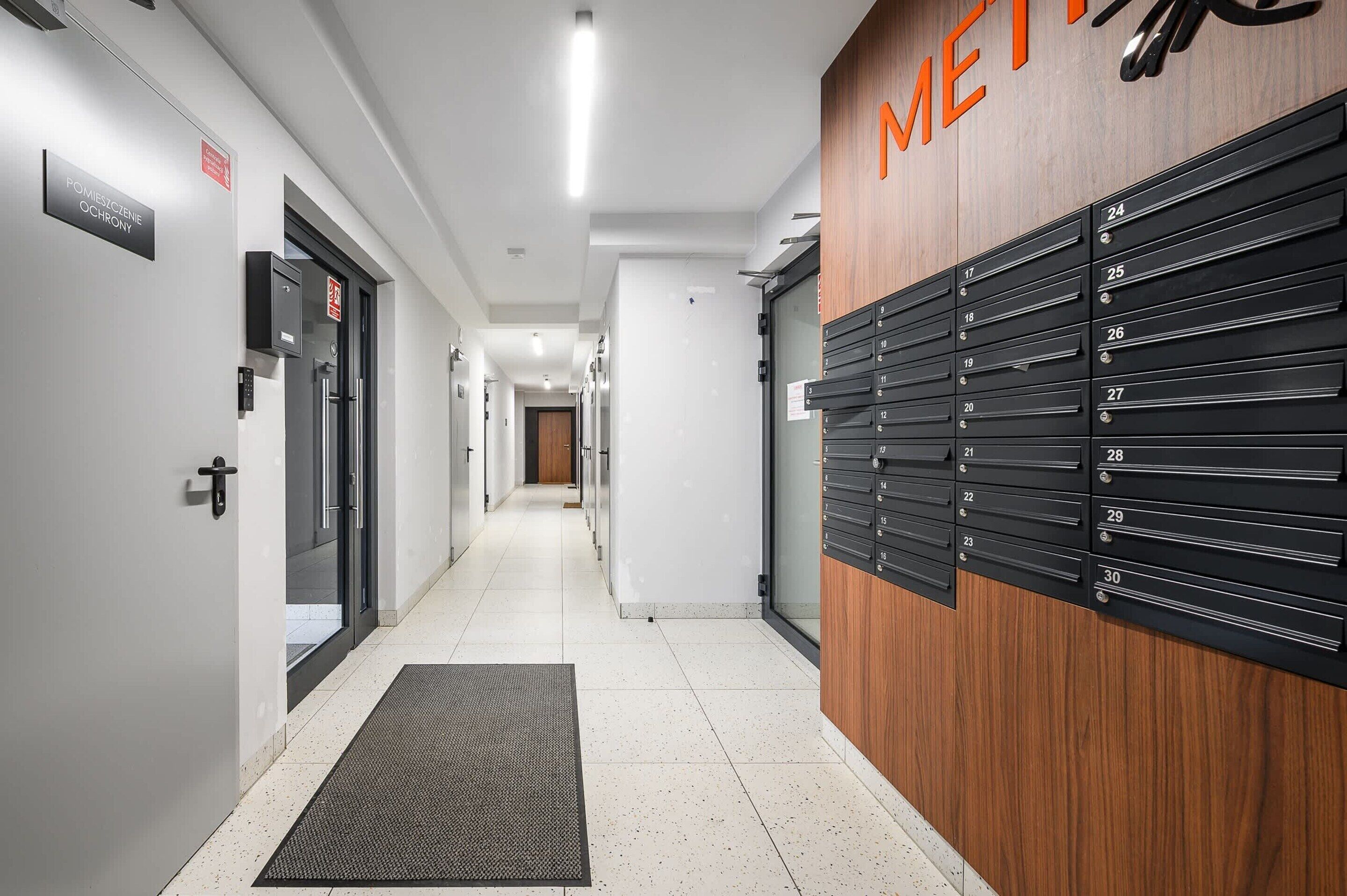 A hotel corridor with a wooden wall displaying room numbers, a fire safety sign, and a door with a handle.