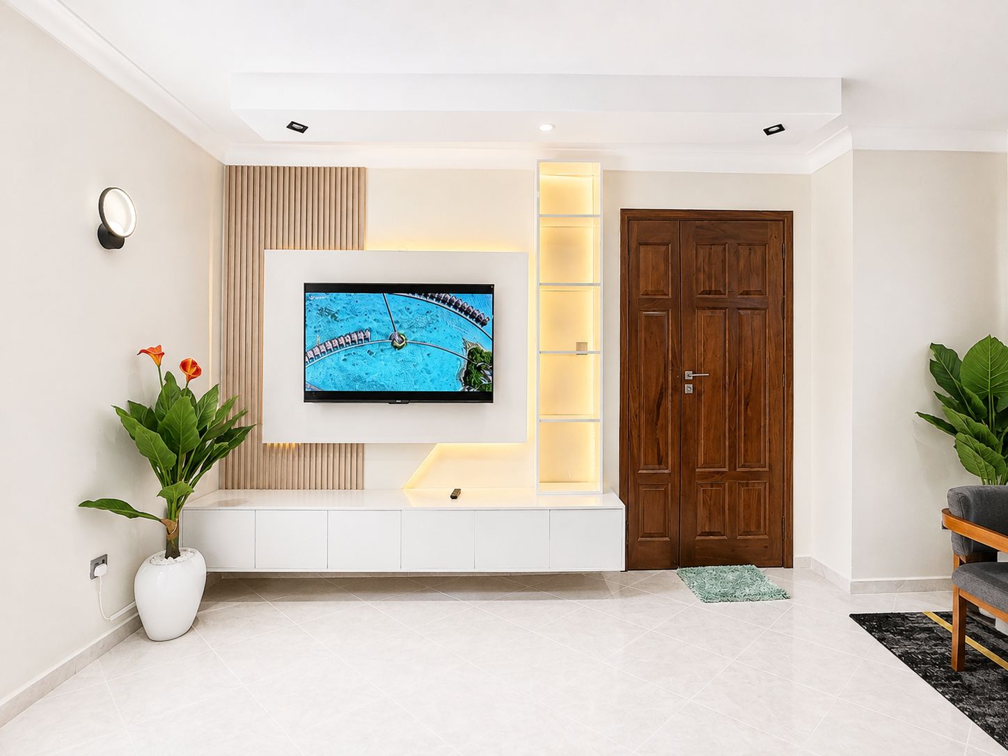 Uma sala de estar moderna com televisão de tela plana fixada em um móvel branco, uma porta de madeira e um vaso com planta.