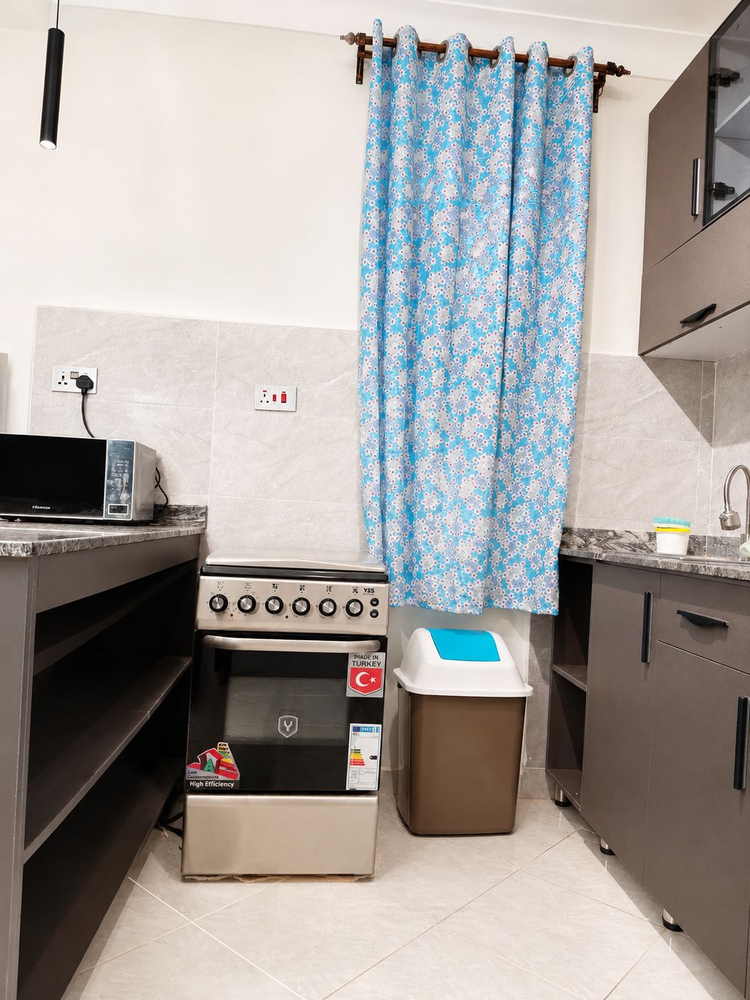 A kitchen with a stove, a trash bin, and a power outlet.