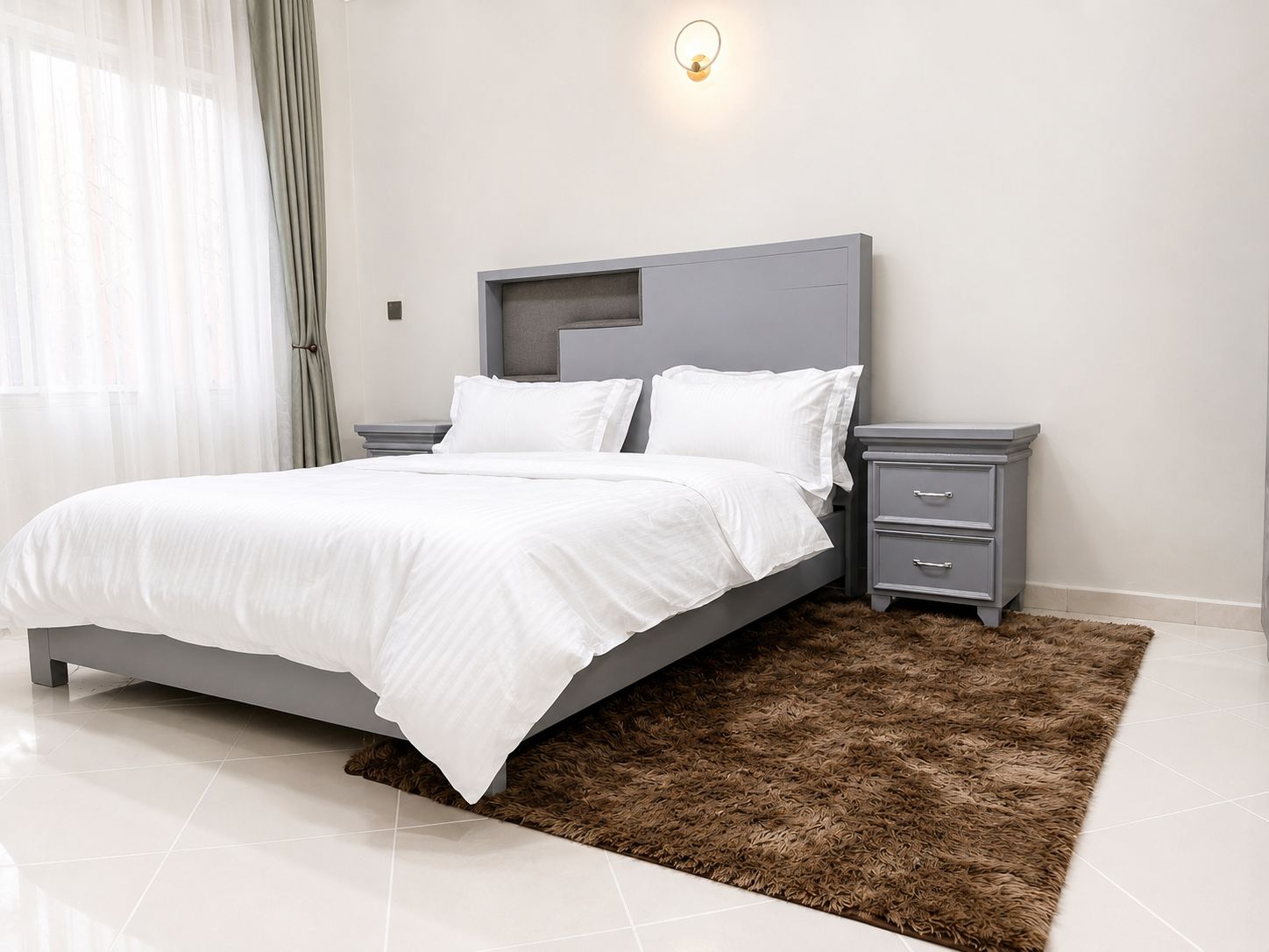 A modern bedroom with a bed, bedside tables, and a wall-mounted light fixture.