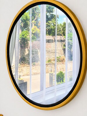 Una ventana redonda con marco amarillo, que ofrece vista a un muro de piedra y follaje.