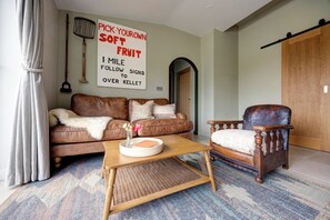 A cozy living room with a brown sofa, a wooden coffee table, a vintage armchair, and a wall sign. - Luxury Converted Stable Cottage | Lake District | EV Charger & Private Patio (Carnforth)