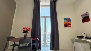 Een kamer met een eettafel, stoelen, een kleine koelkast en een raam met gordijnen.