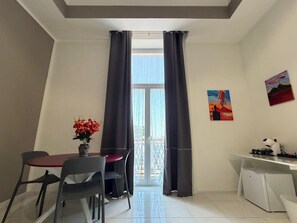 Una habitación con una mesa de comedor, sillas, un refrigerador pequeño y una ventana con cortinas.