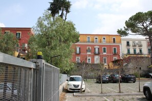 Zona residencial con edificios de varios pisos, coches aparcados y un área cercada con un árbol.