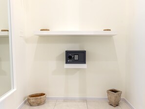 Una habitación con pared blanca, una caja fuerte anclada y dos cestas en el suelo.