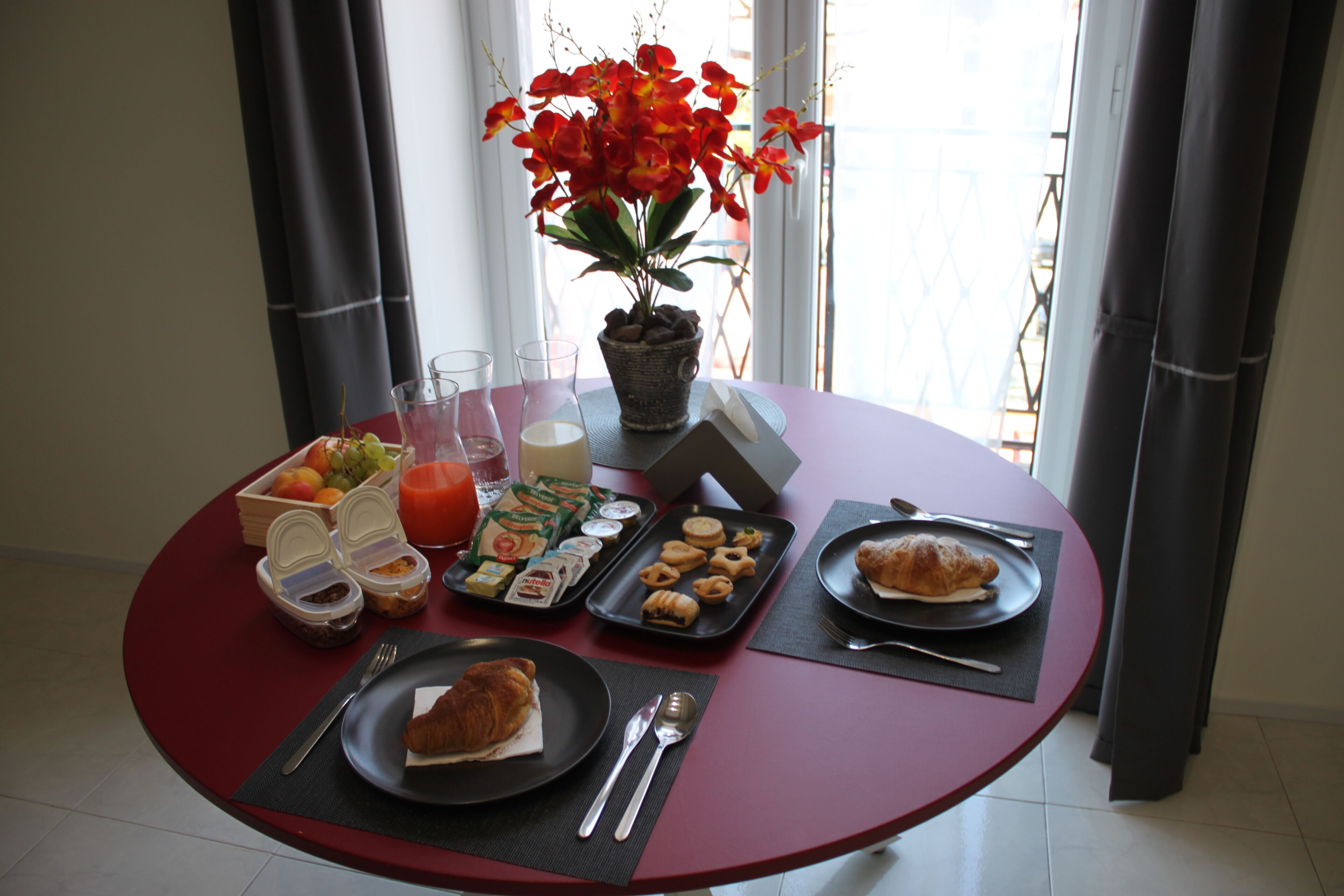 Une table de petit-déjeuner avec un croissant, une assiette de viennoiseries, un saladier de fruits et divers condiments.
