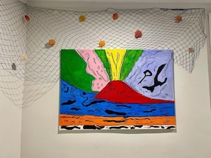 Un colorido cuadro de un volcán con el mar al frente, colgado en una pared.