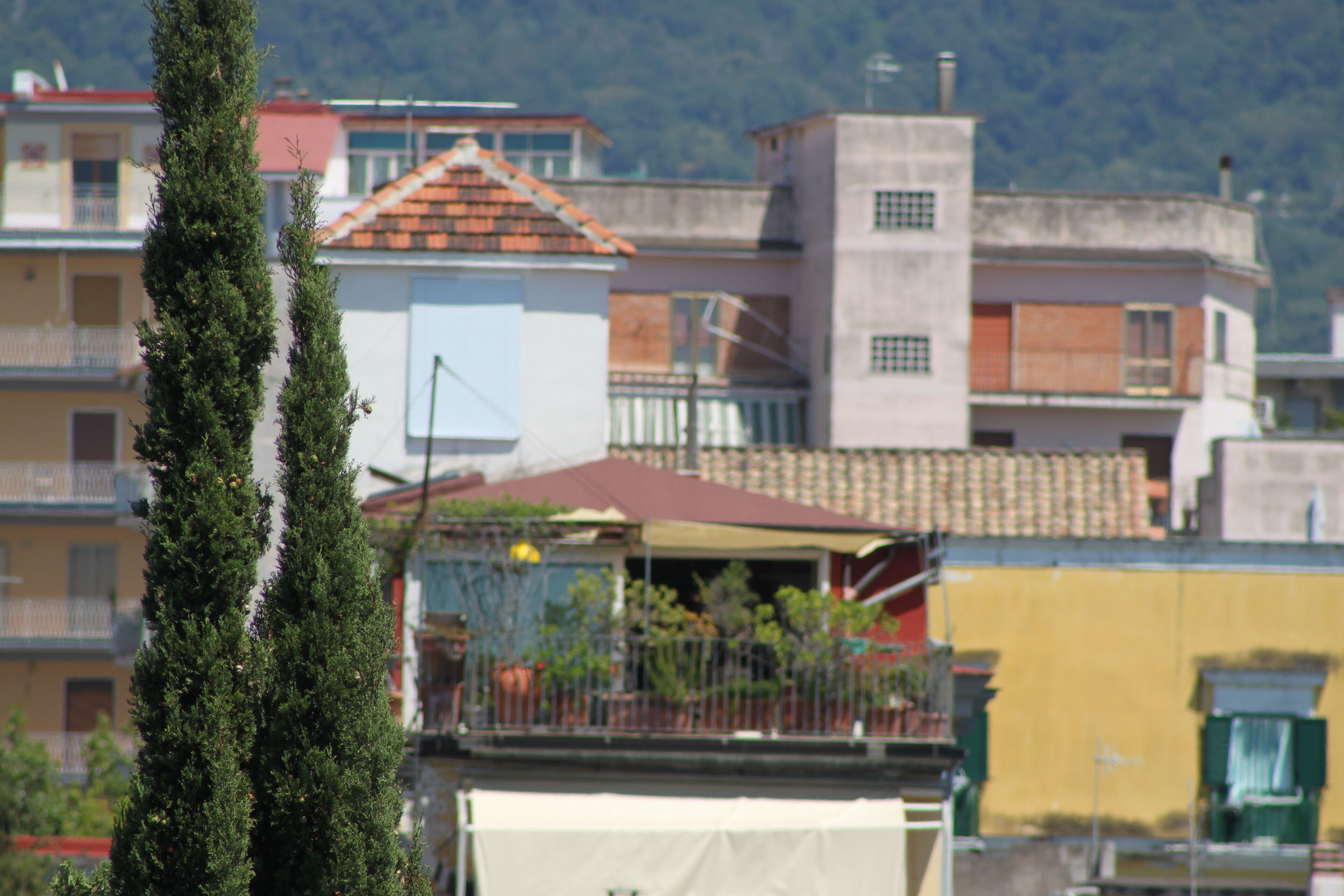 Un immeuble résidentiel avec un toit recouvert de tuiles rouges, un balcon et un mur blanc.