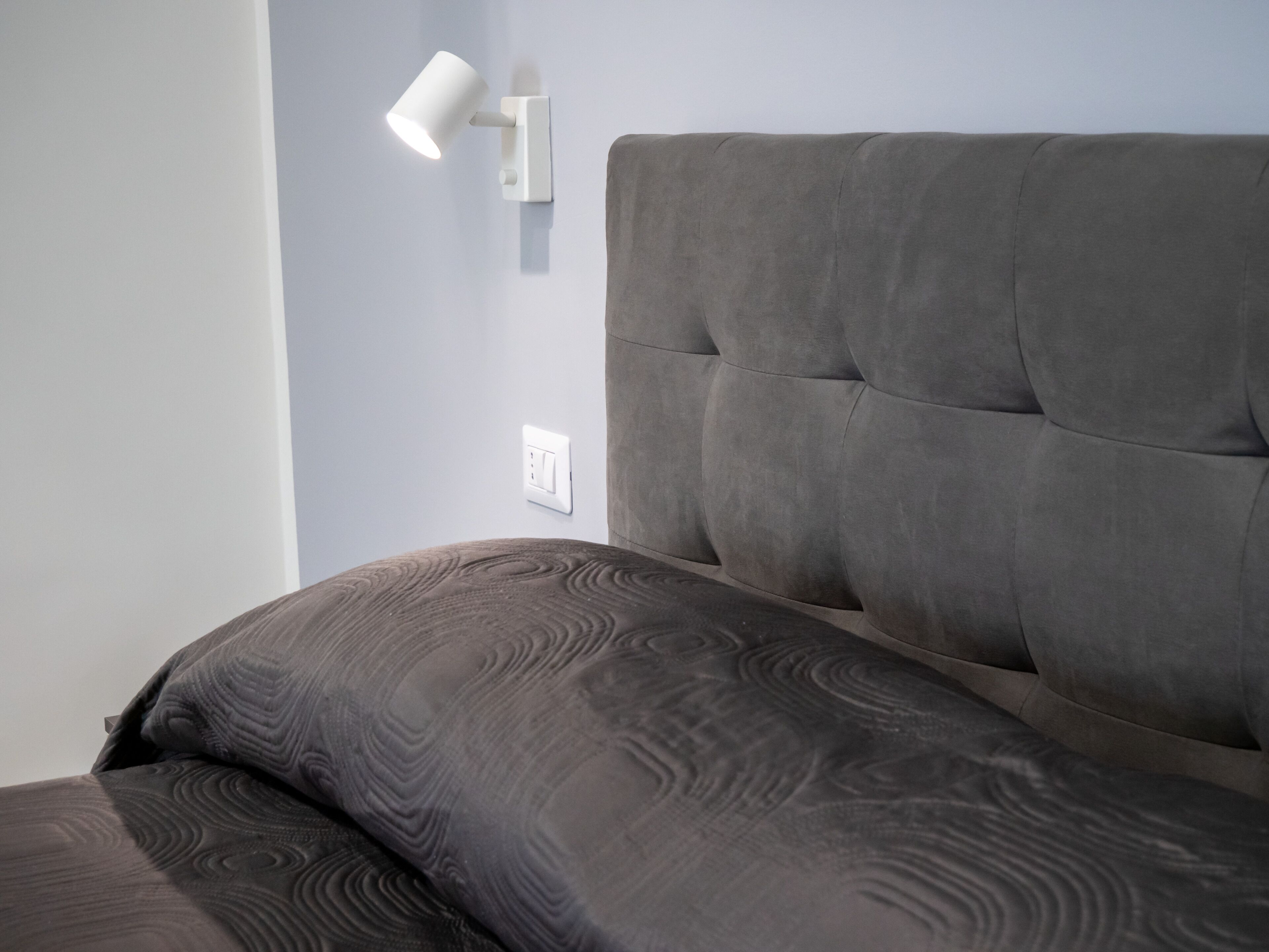 Una cama con cabecera, una lámpara de pared y un enchufe.