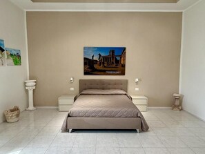 Un dormitorio con una cama grande, dos mesitas de noche, un cuadro en la pared y suelo de baldosas.