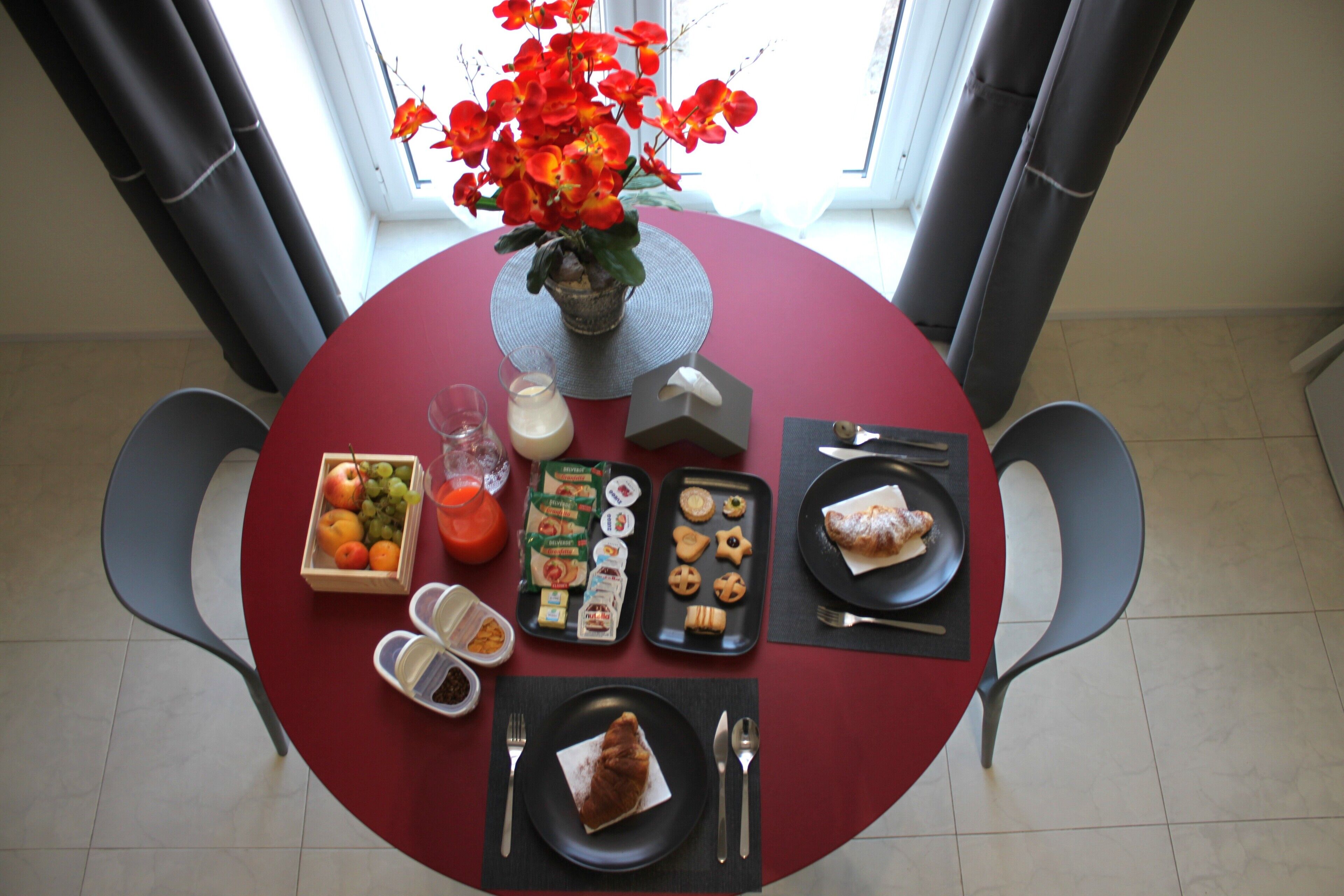 A dining table with a red tablecloth, a vase with red flowers, and various food items and drinks.